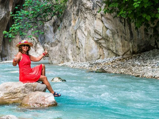 Woman in a red dress sitting on a rock in a turquoise river