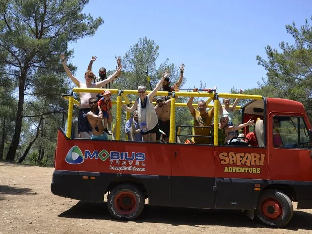 Excited tourists waving from a red open-air safari bus in the woods