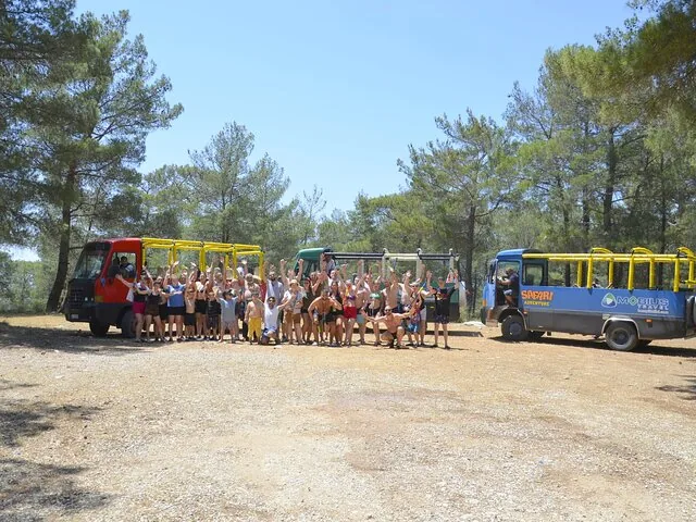 Large group of people posing in front of three colorful safari buses