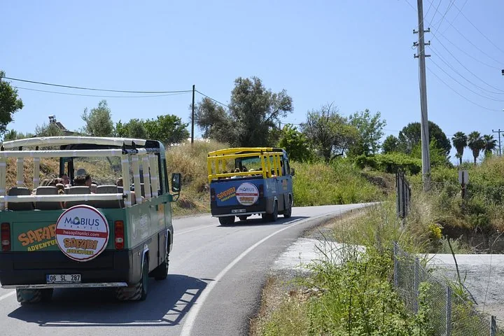 Two open-air safari buses driving along a rural road