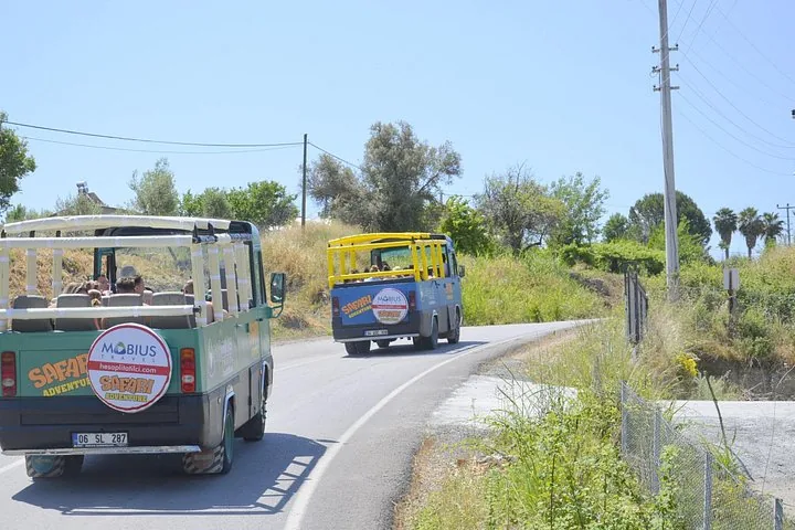 Two safari buses driving on a paved road through a rural area